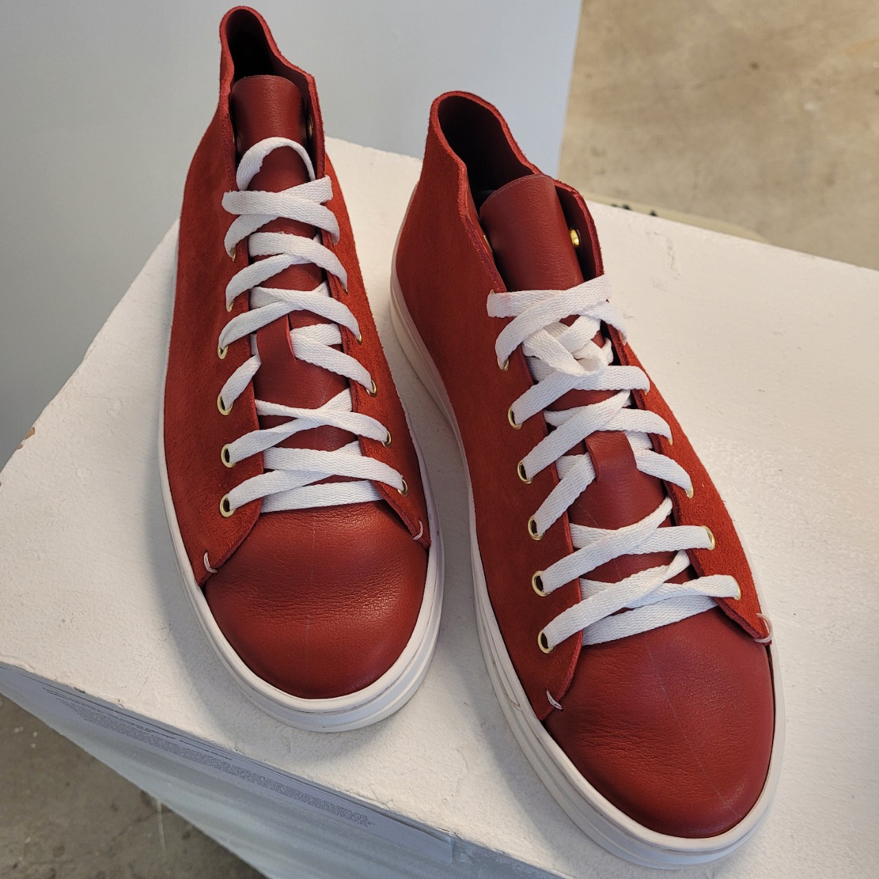 Home made red canvas shoes sittin gon a pedestal.